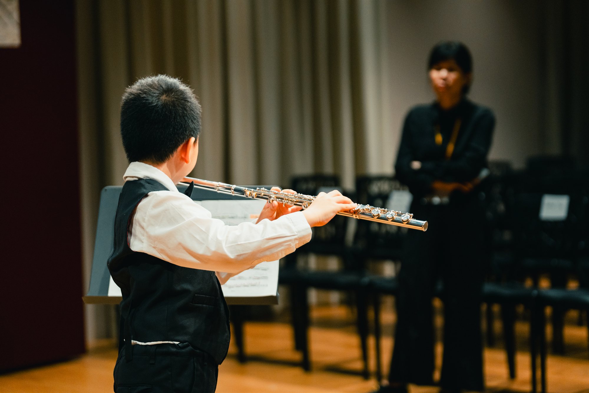 A young student performing on flute while their King's Flute Choir teacher listens